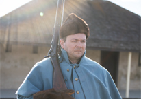 A reenactor in period garb with rifle standing outside a historical building at Fort Hartsuff