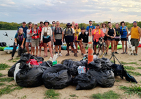 Group of kayak cleanup volunteers posing by pile of full trash bags they collected