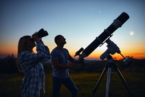 Couple looking through telescopes after the sun has set