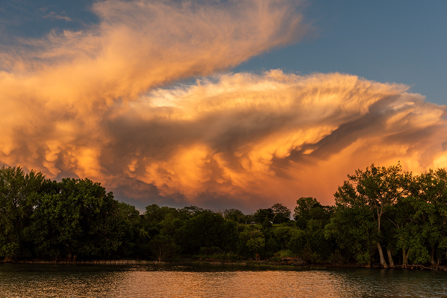 A dramatic orange storm cloud hangs over the water and trees at Sherman Reservoir.