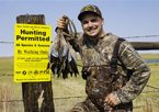 Hunter posing with teal he harvested next to an Open Fields and Waters sign