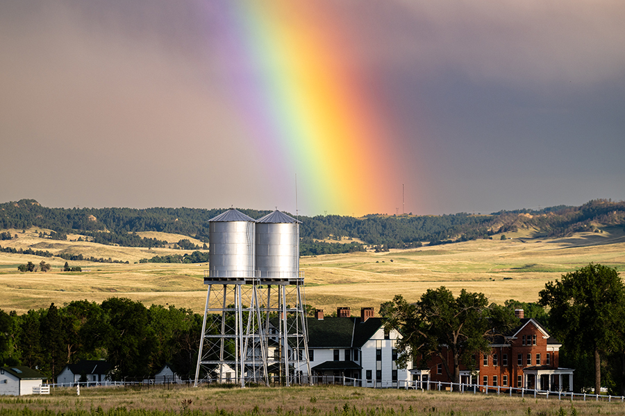 A large, vivid rainbow appears over the lodging and water towers at Fort Robinson State Park.