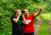 Two young women looking for birds through binoculars, smiling and pointing