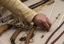 A living history reenactor picks up an arrow among other old-fashioned tools.