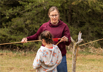 An instructor helps a girl use an atlatl