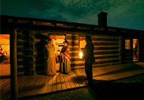 Reenactors gather outside a doorway at Fort Atkinson at night, lit by candlelight