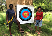 A couple stands next to an outdoors archery target