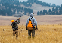 A youth takes aim at a pheasant while a mentor watches