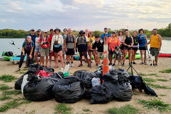 Group of volunteers at a beach posing by bags full of trash they collected by kayak