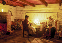 A living history interpreter spins wool in a candlelit room at Fort Atkinson State Historical Park.