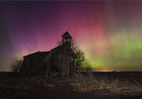 An aurora above the silhouette of an abandoned barn.