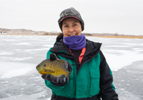 A woman holds up a fish caught through the ice