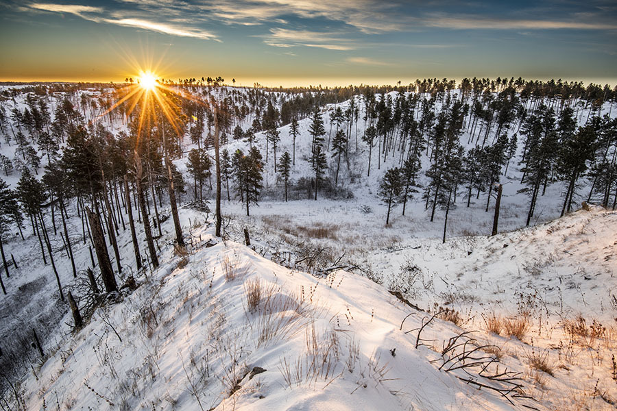 Sunrise over a forested landscape at Chadron State Park in winter.