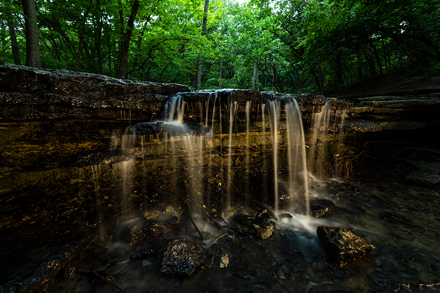 Stone Creek Falls at Platte River State Park at night, a small waterfall with trees in distance.