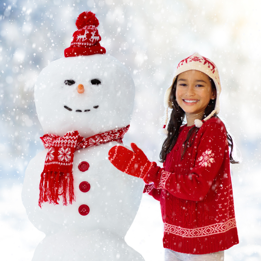 A girl poses next to the snowman she built while snow is falling.