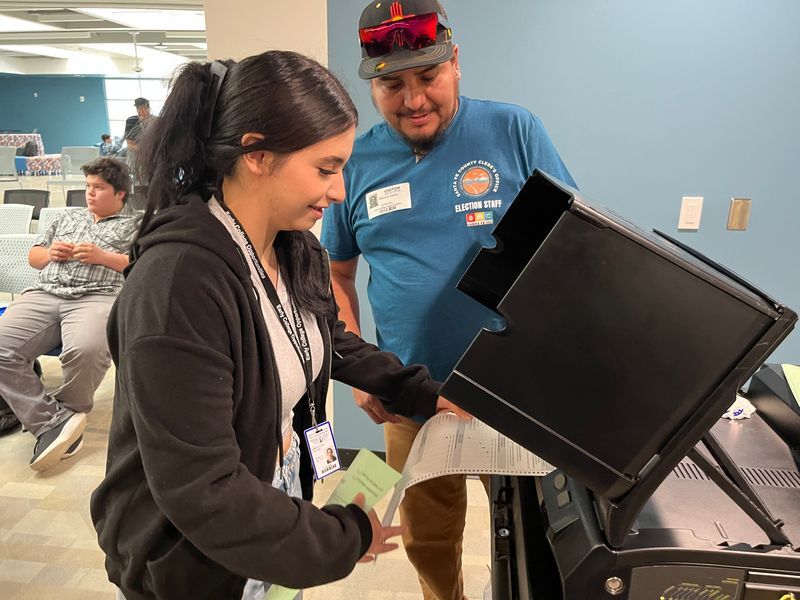 Picture of a staff member helping a high schooler cast a ballot