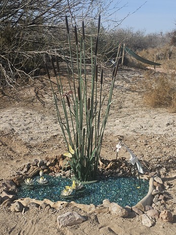 Metal and glass sculpture of cattails and an egret in a small pond.