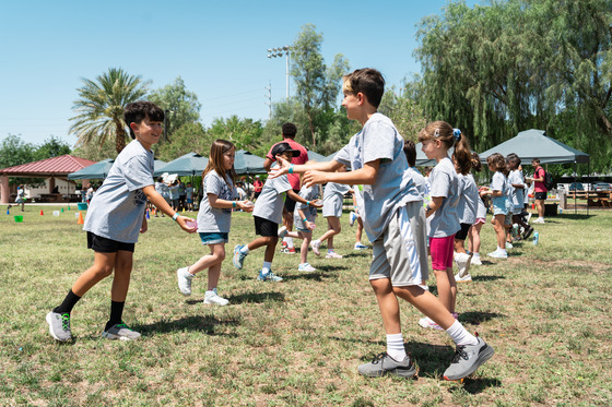 summer camp - A group of children are playing outdoors on a grassy field under a clear sky.