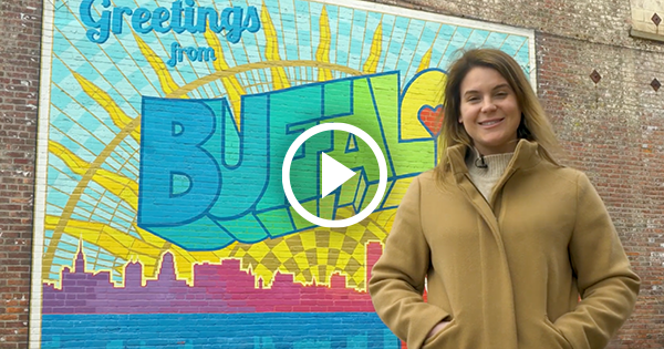 Play button image of woman standing in front of Buffalo mural.