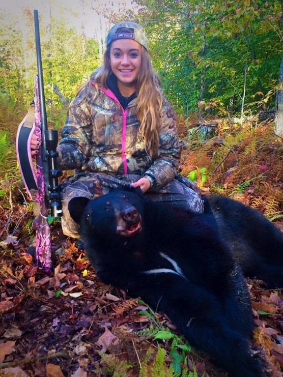 A young woman posing with a blackbear and the gun she shot it with