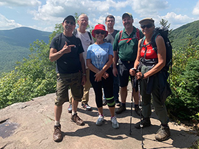 A group of hikers ontop of a rocky quarry with the catskill mountains in the background