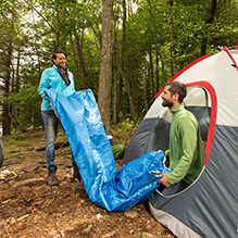 A couple unrolling their blue sleeping bag in a tent at a DEC campground
