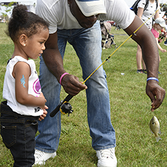 A father teaching his young daughter how to take a fish off the hook at the 2019 state fair