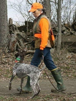 a woman in hunting clothes walks her dog in the woods