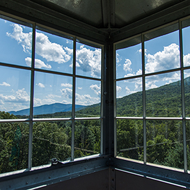 A landscape view of inside the Upper Esopus Fire Tower looking out the windows to a mountainous view of Mt. Tremper