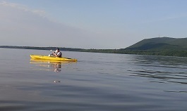 A man in a yellow kayak paddles on the Hudson River with mountains in the background.