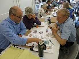 A group of people gather around site maps on a long table in a room.
