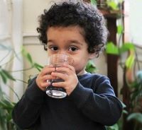 A young child with curly dark hair drinks a glass of water