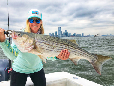 Angler holding striped bass in front of New York City skyline