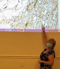 A woman with a face mask stands in front of a map projected on the wall.