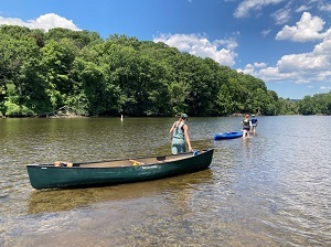 people pull canoes while wading into a pond