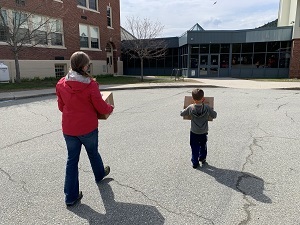 a woman and a small boy carry boxes in a parking lot