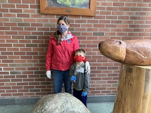 a woman and a small boy stand in a school while wearing masks. the boy holds a tree seedling