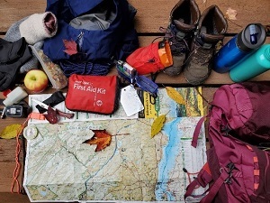 hiking supplies including a backpack, map, snacks, first aid kit, watter bottles, compass, and more