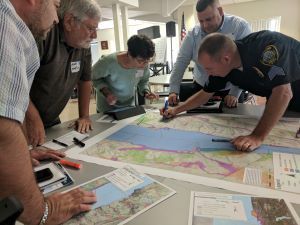 A group of 5 people gather around a table looking at large maps that show the Hudson River.