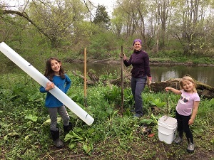 a woman and two girls hold tree-planting supplies in the forest