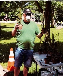 a man in a mask holds up seedlings at the giveaway event outside