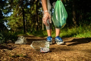 a gloved hand picks up plastic litter on a trail