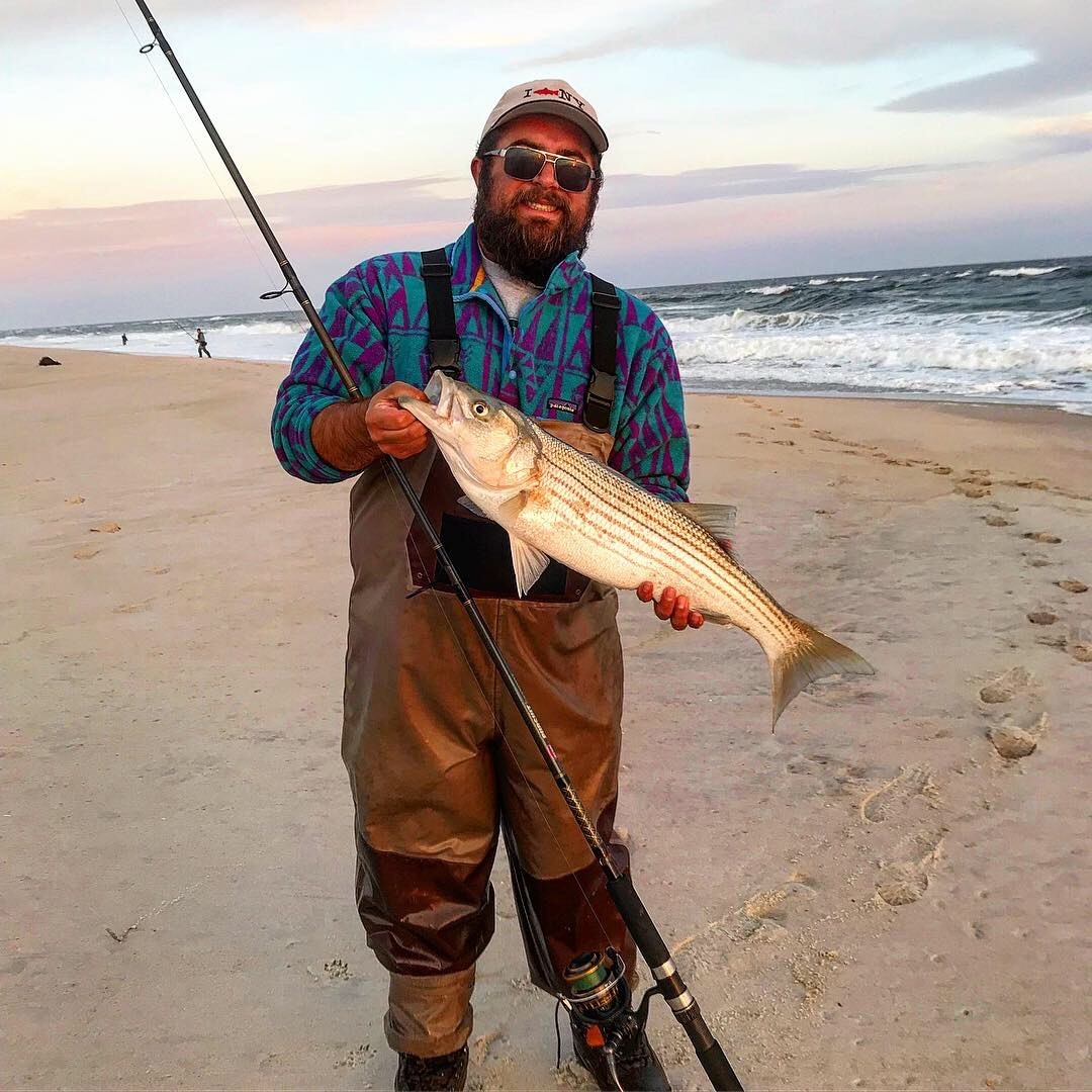 Surfcaster holding striped bass on ocean beach