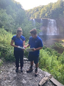 two people in blue shirts look at paperwork near a waterfall