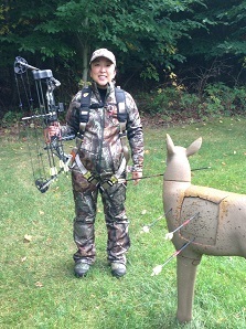 A young woman holding a bow demonstrates a properly fitted treestand harness 