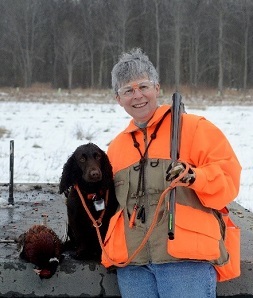 Man poses with his dog and a harvested pheasant in front of a snowy field