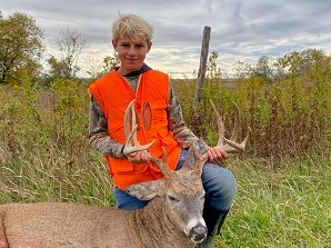 Youth hunter in a blaze orange vest poses with a harvested whitetail buck
