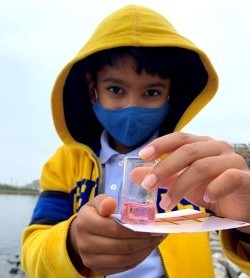 A young boy wearing a mask holds a tube of colored water.