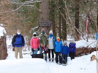 A family standing in the snow waiting to go on a hike holding a dog on a dog leash