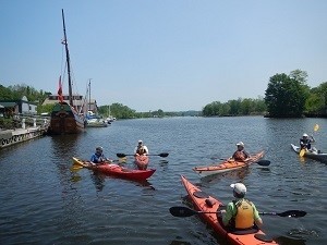 Several kayakers paddle on the Hudson near Kingston on a sunny day.